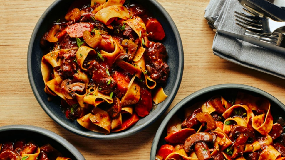 Trois bols de veau bourguignon accompagné de pâtes.