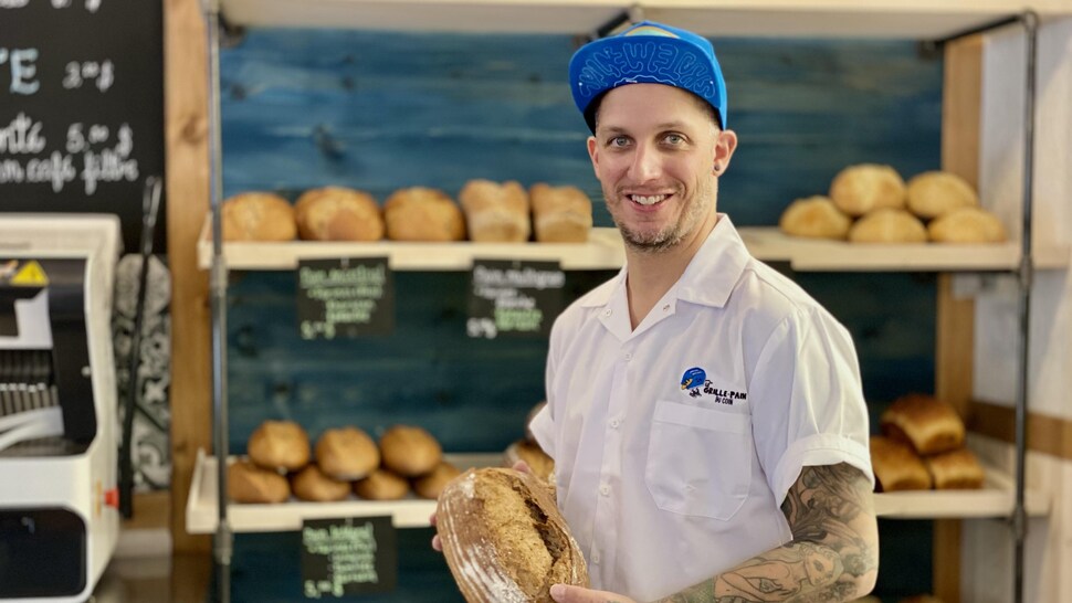 Un homme souriant, tient dans ses mains une miche de pain. 