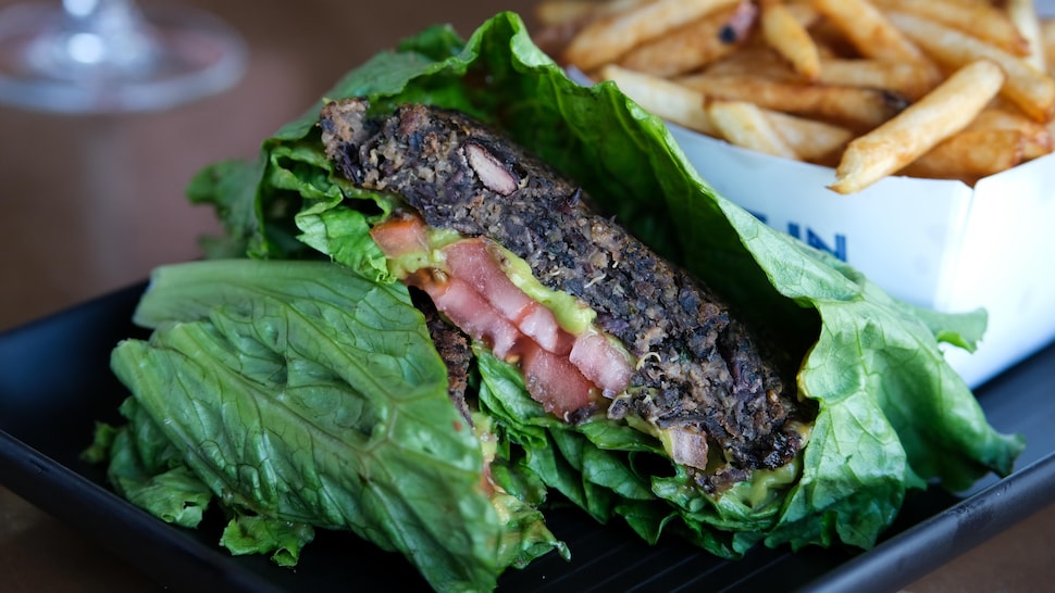 Le burger végétalien est présenté entre deux feuilles de laitues et garni de tomates et d'une purée d’avocat.