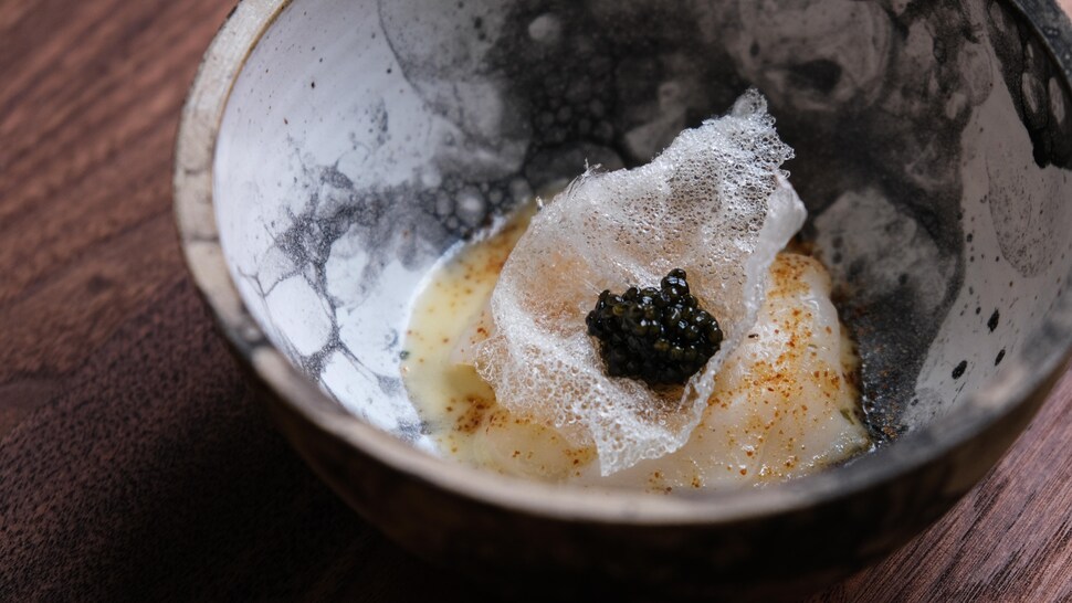 Un plat de pétoncle dans un bol, monté avec une croustille de pomme de terre et du caviar d'esturgeon. 