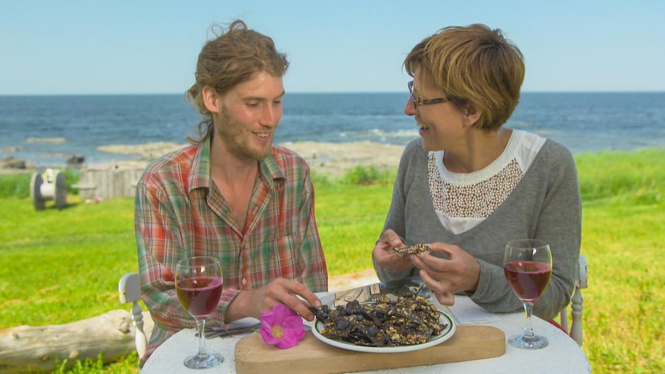 Johane et son invité sont sur le bord de la plage et mange du chocolat à base d'algues.