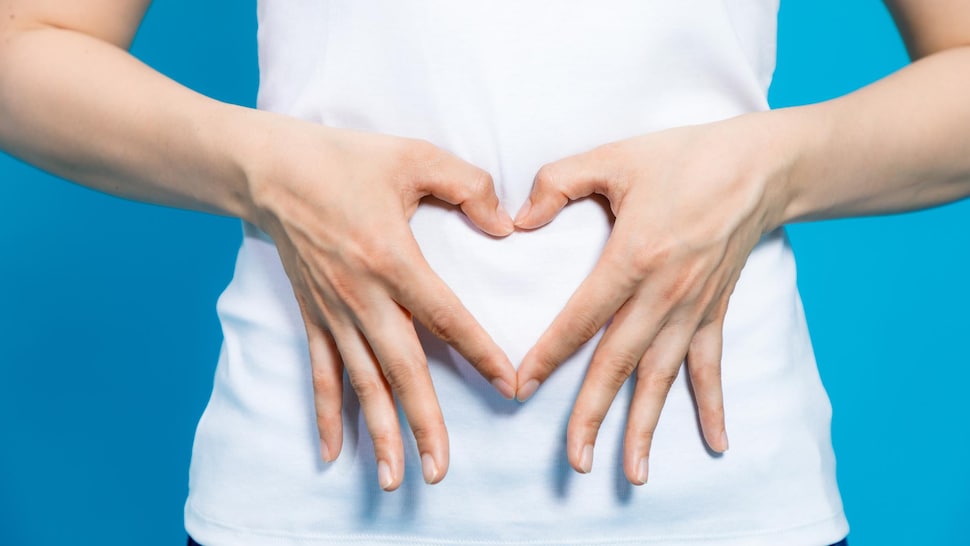 Une femme forme un cœur avec ses mains sur son abdomen.