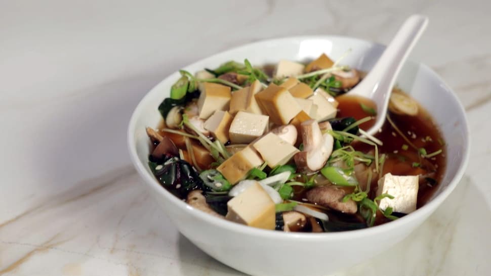 Une soupe asiatique contenant des champignons, des herbes et du tofu fumé.
