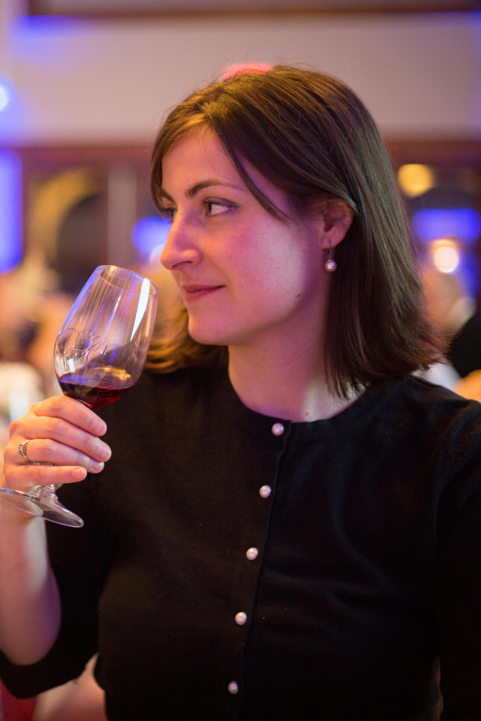 Une femme approche un verre de vin rouge de son visage. 