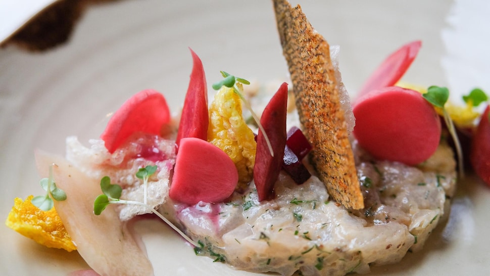 Un tartare de doré avec des légumes colorés et une chip de peau de saumon. 