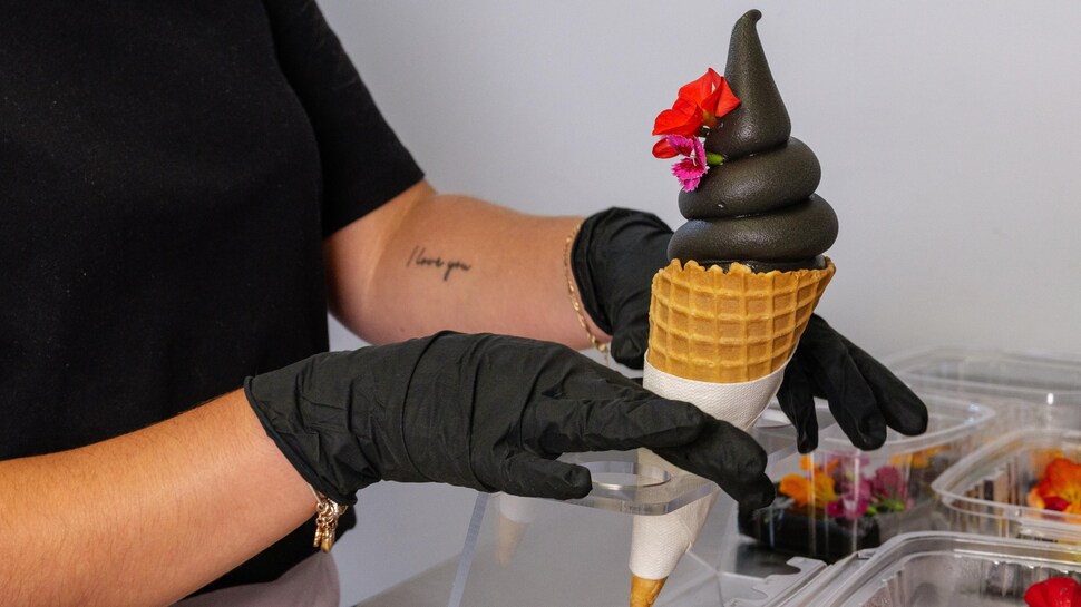 Une jeune femme dépose des fleurs sur un cornet de crème glacée noire. 