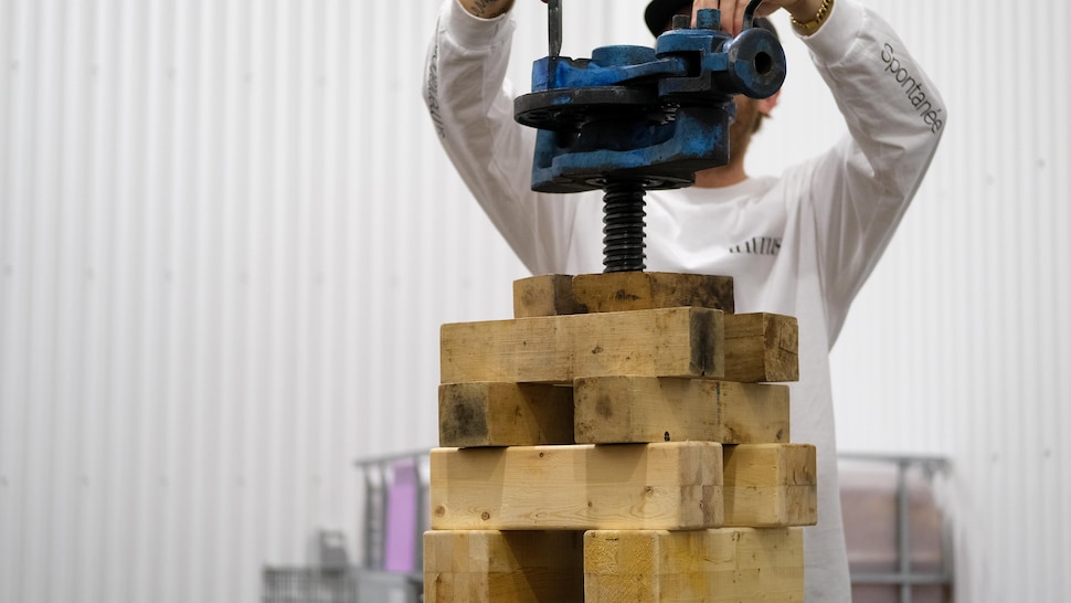 Une personne installe un levier sur des morceaux de bois afin d'activer une presse manuelle. 
