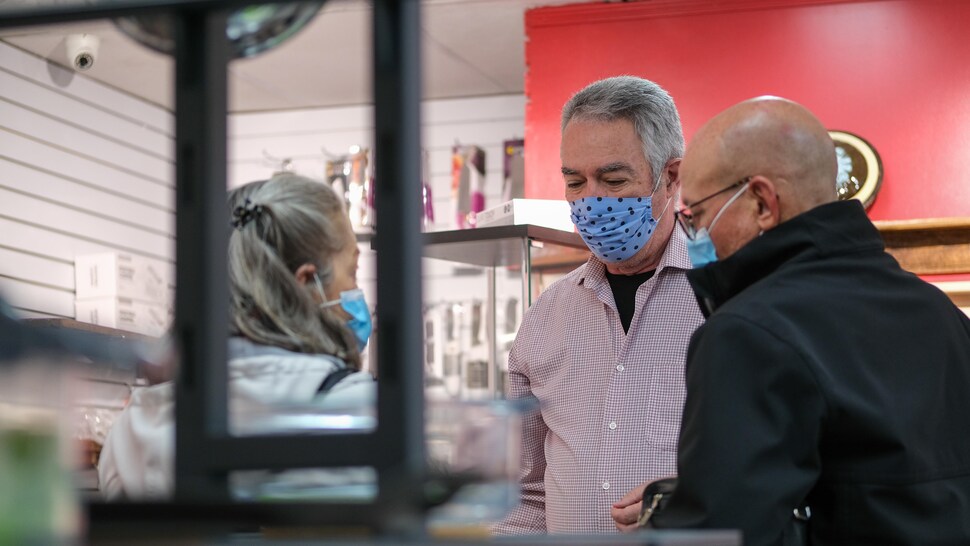 Un homme portant un couvre-visage conseille une femme et un homme dans l'achat de couteaux. 