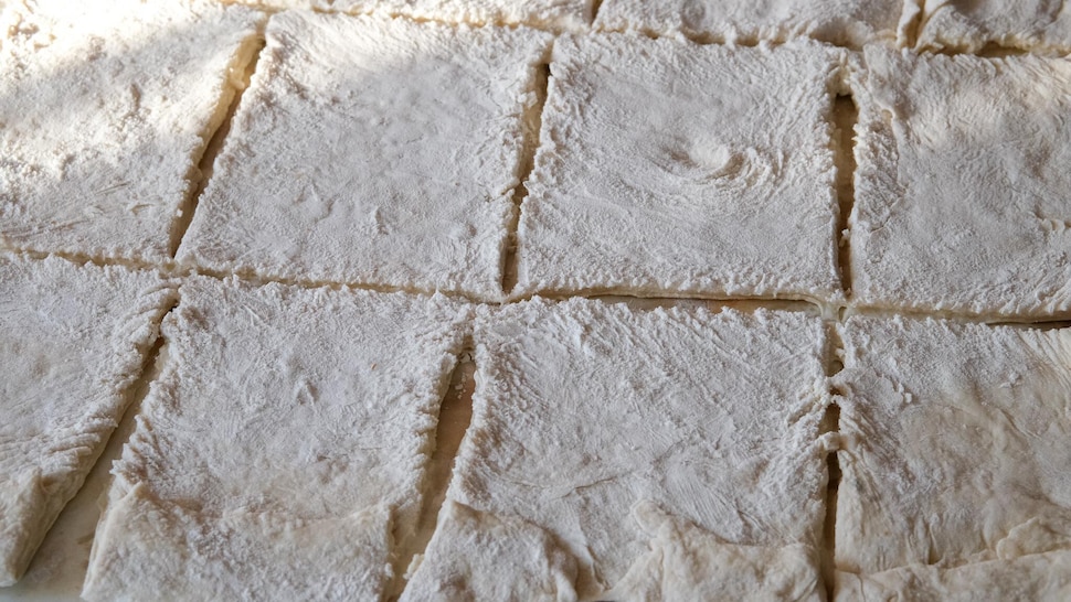 Des carrés de pâte sur une surface farinée. 
