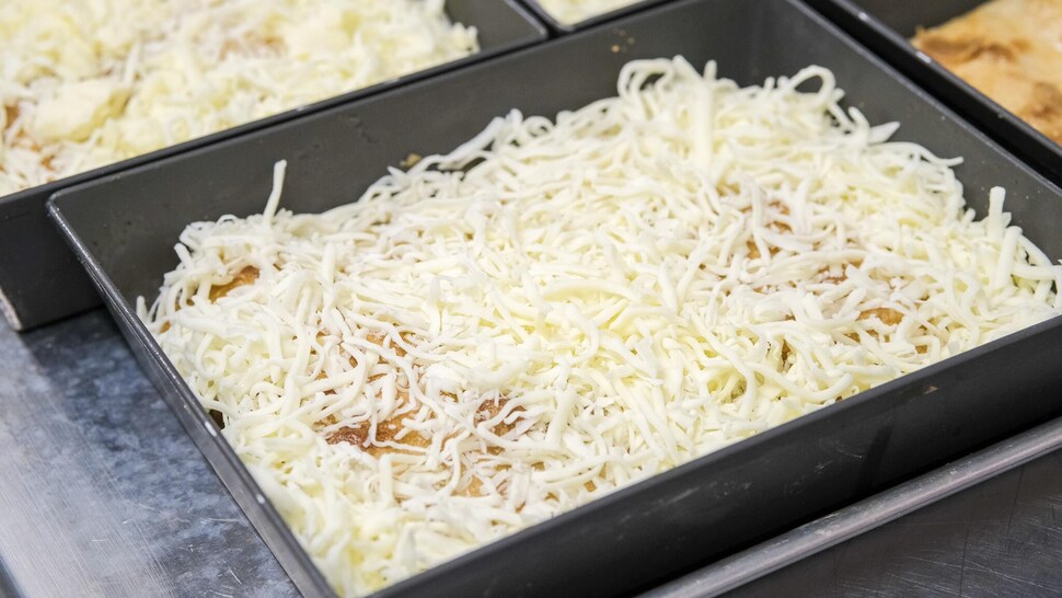 Hand shredded cheese on a rectangular pizza crust. 