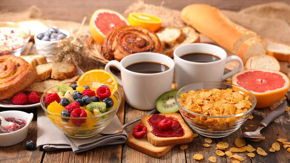 Table remplie de fruits, de café, de céréales, de pain et de viennoiseries.