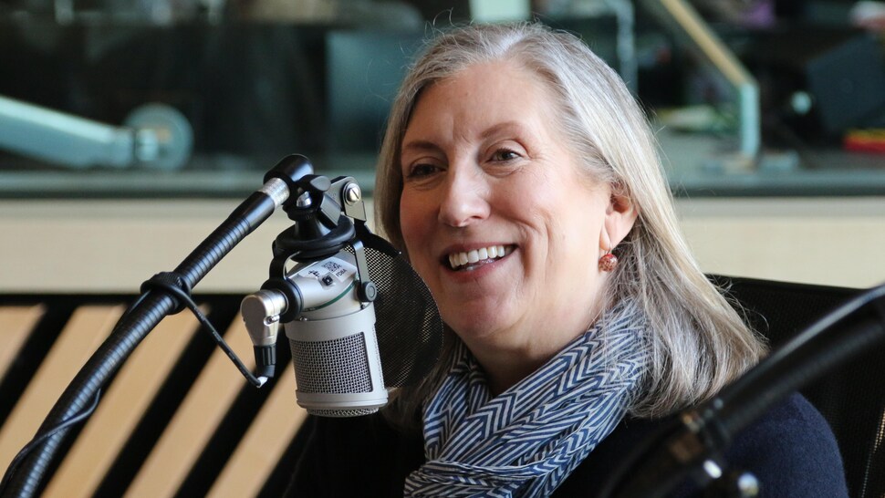 Une femme parle en souriant dans un micro, dans un studio de radio. 