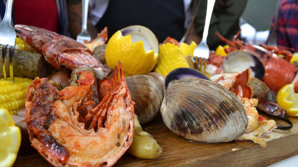 Des fruits de mer, avec du citron et des légumes sur une planche de bois.