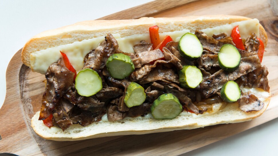 Un pain coupé en deux ouvert avec des tranches de bœuf, du fromage, des poivrons et des tranches de concombres marinés.