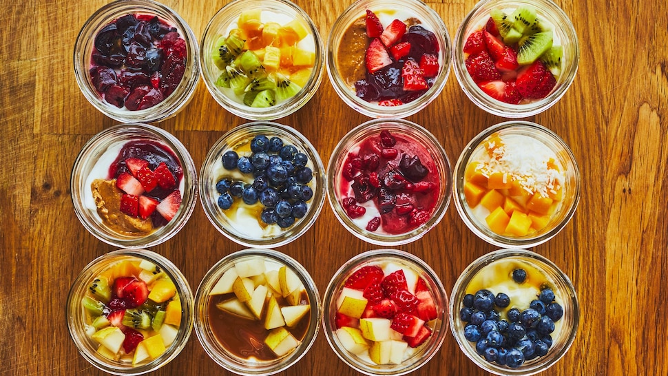 Douze pots en verre, remplis de yogourt garni d'une variété de fruits, sont disposés symétriquement sur une table.