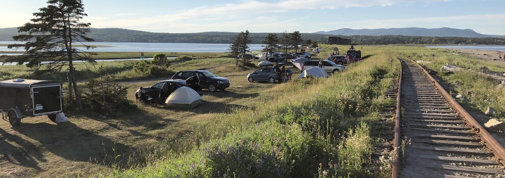 Des véhicules et des tentes sont installés entre une plage et un chemin de fer à Douglastown, en Gaspésie.