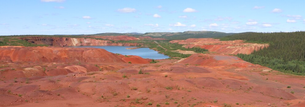 Un paysage minier de terre rougeâtre avec un grand lac et une forêt.