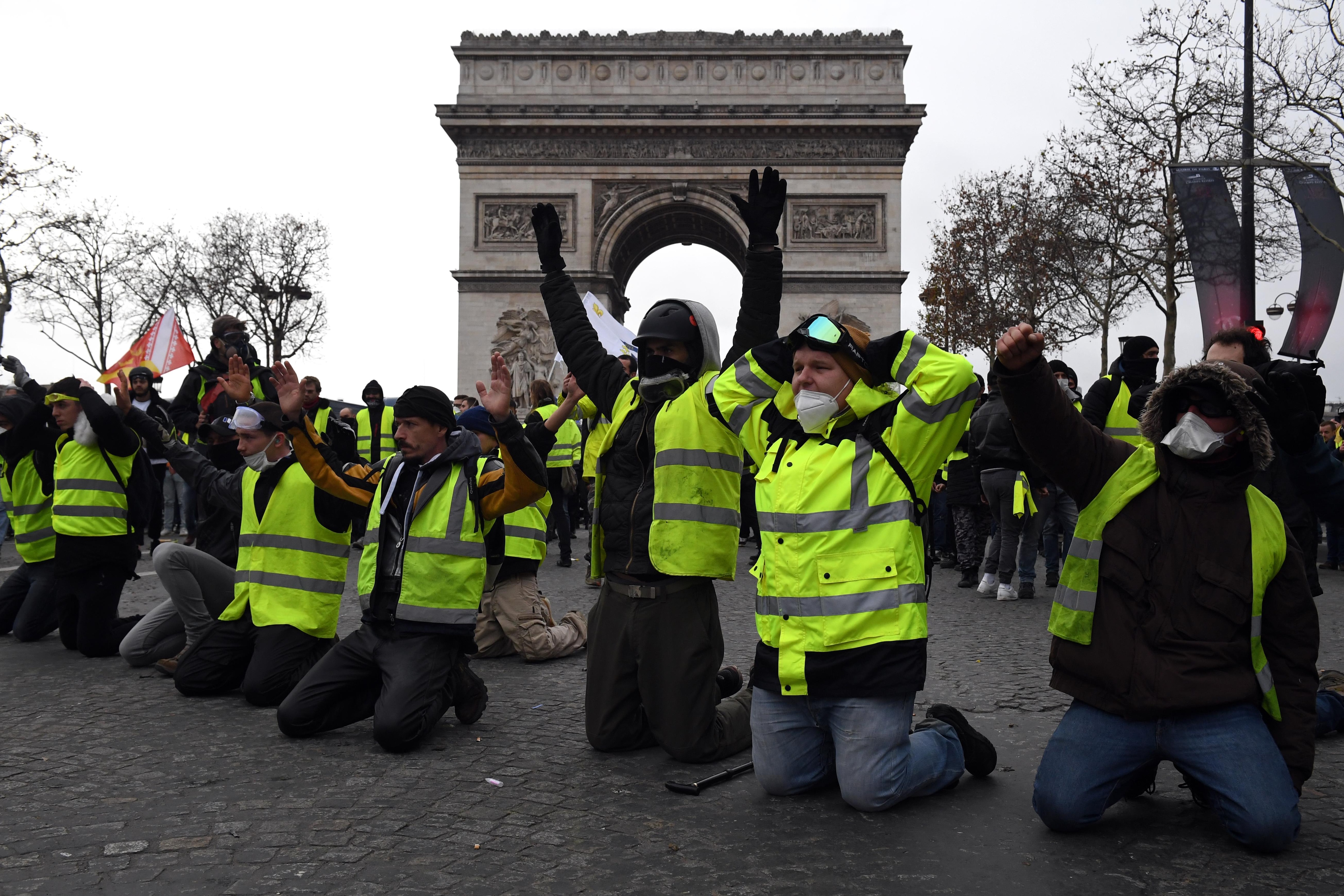 Des hommes en gilets jaunes à genoux devant l'Arc de Triomphe. 