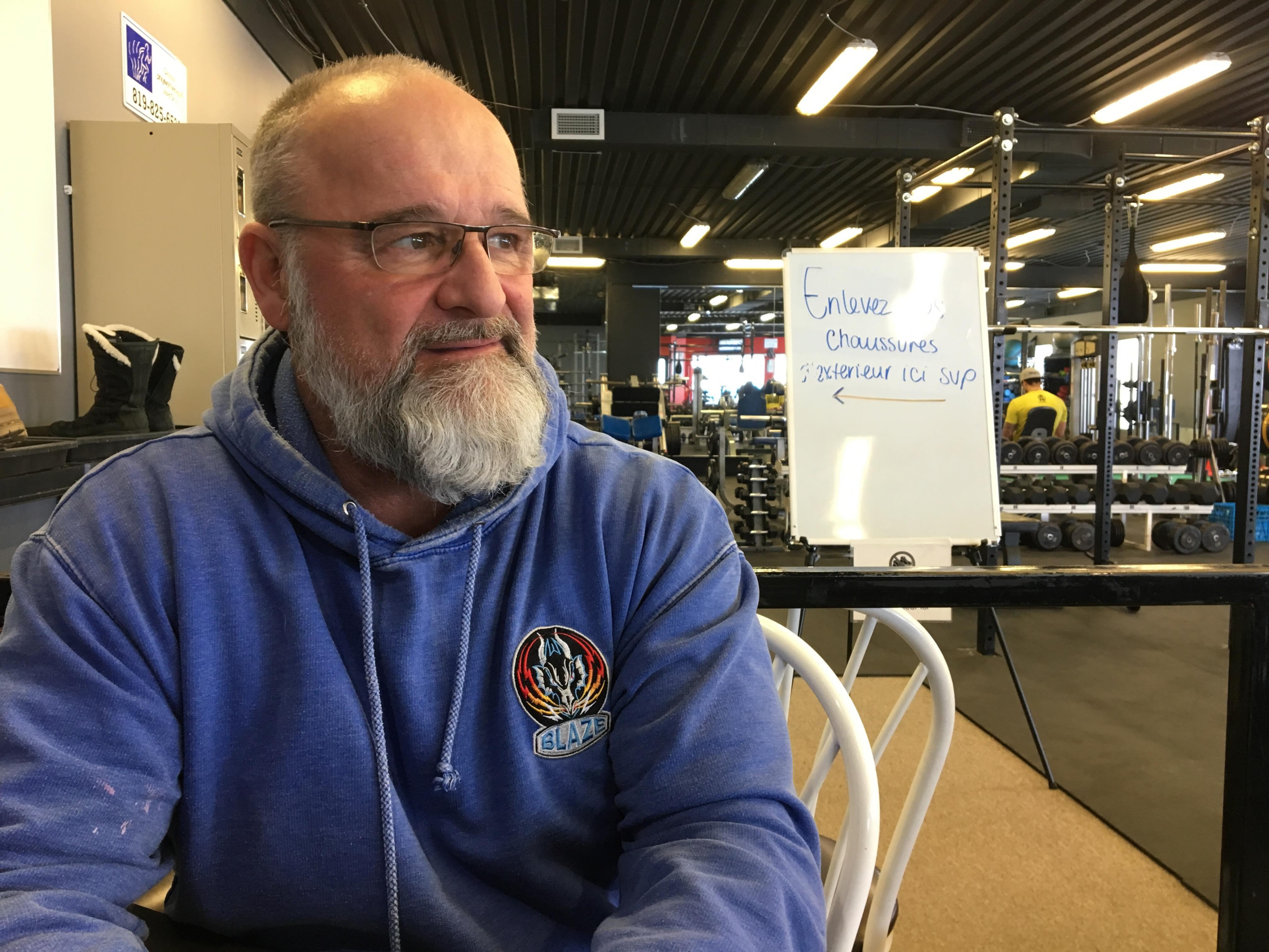 Un homme portant des lunettes et une barbe regarde au loin dans une salle de conditionnement physique.