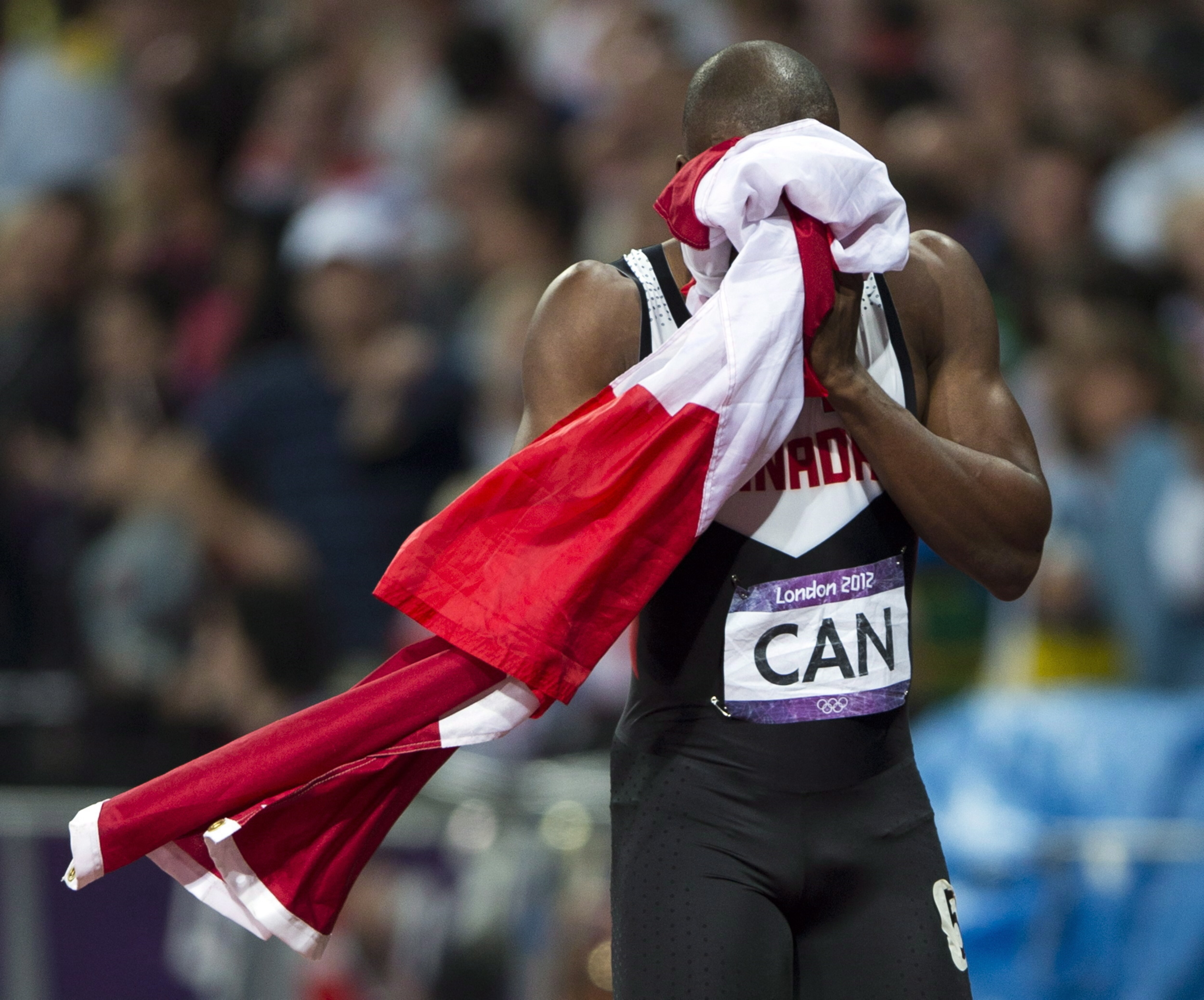 Le sprinteur se cache le visage dans le drapeau du Canada après une course olympique.