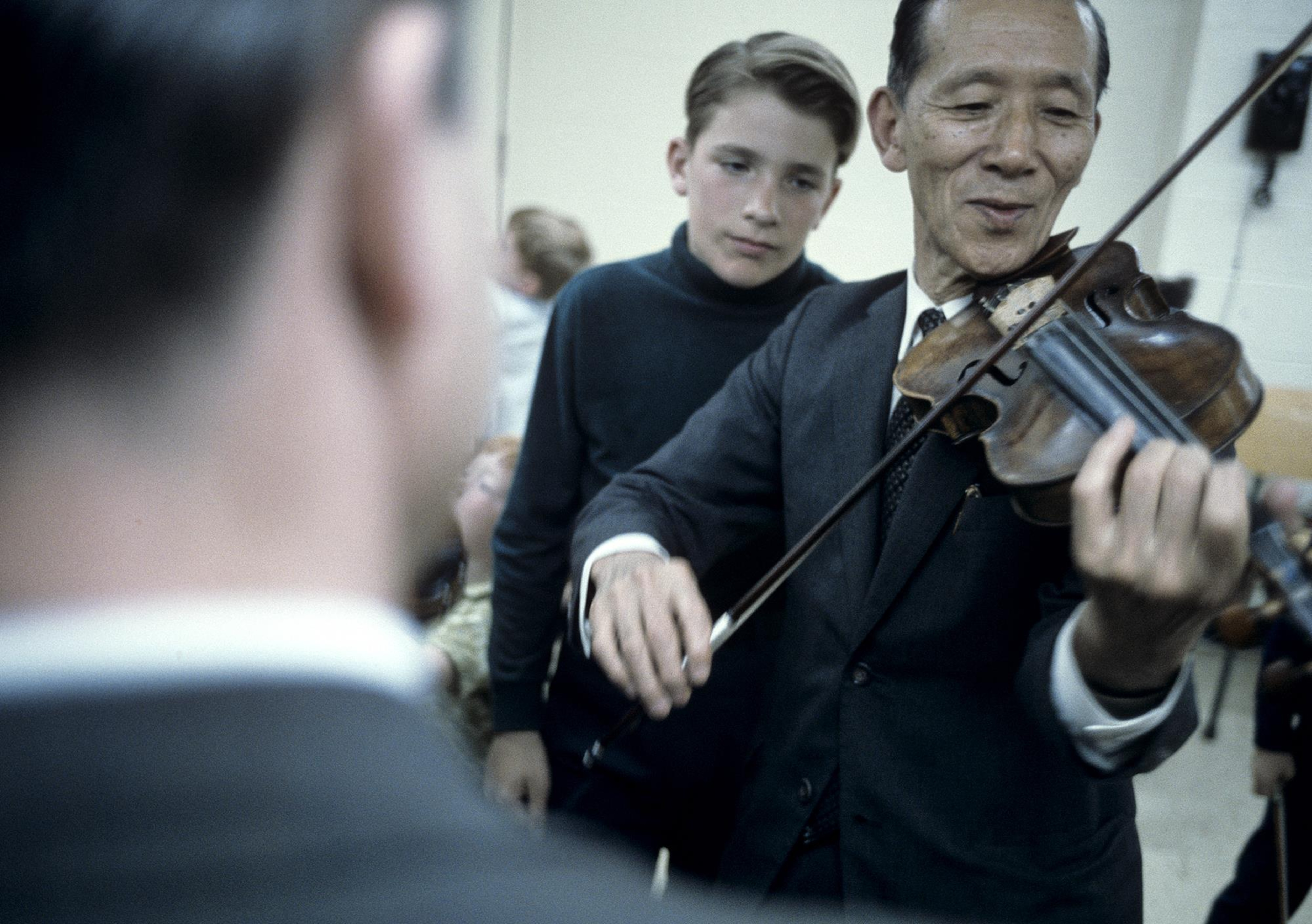 Un professeur de musique avec un violon entre les mains est devant un jeune garçon.