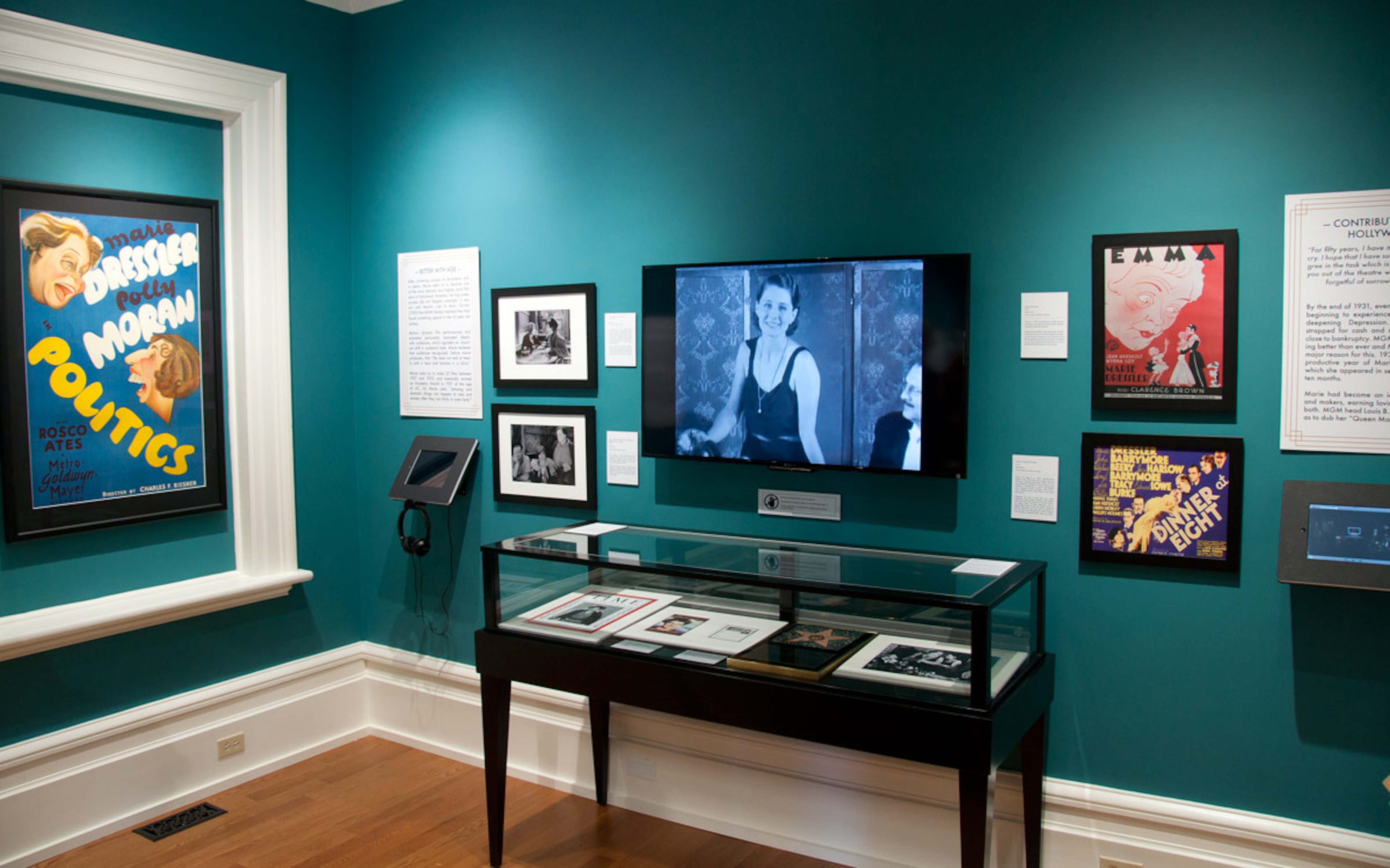 Des affiches aux murs, une vitrine avec des photos à l'intérieur. un écran de télévision avec un film qui est diffusé, un écran interactif.