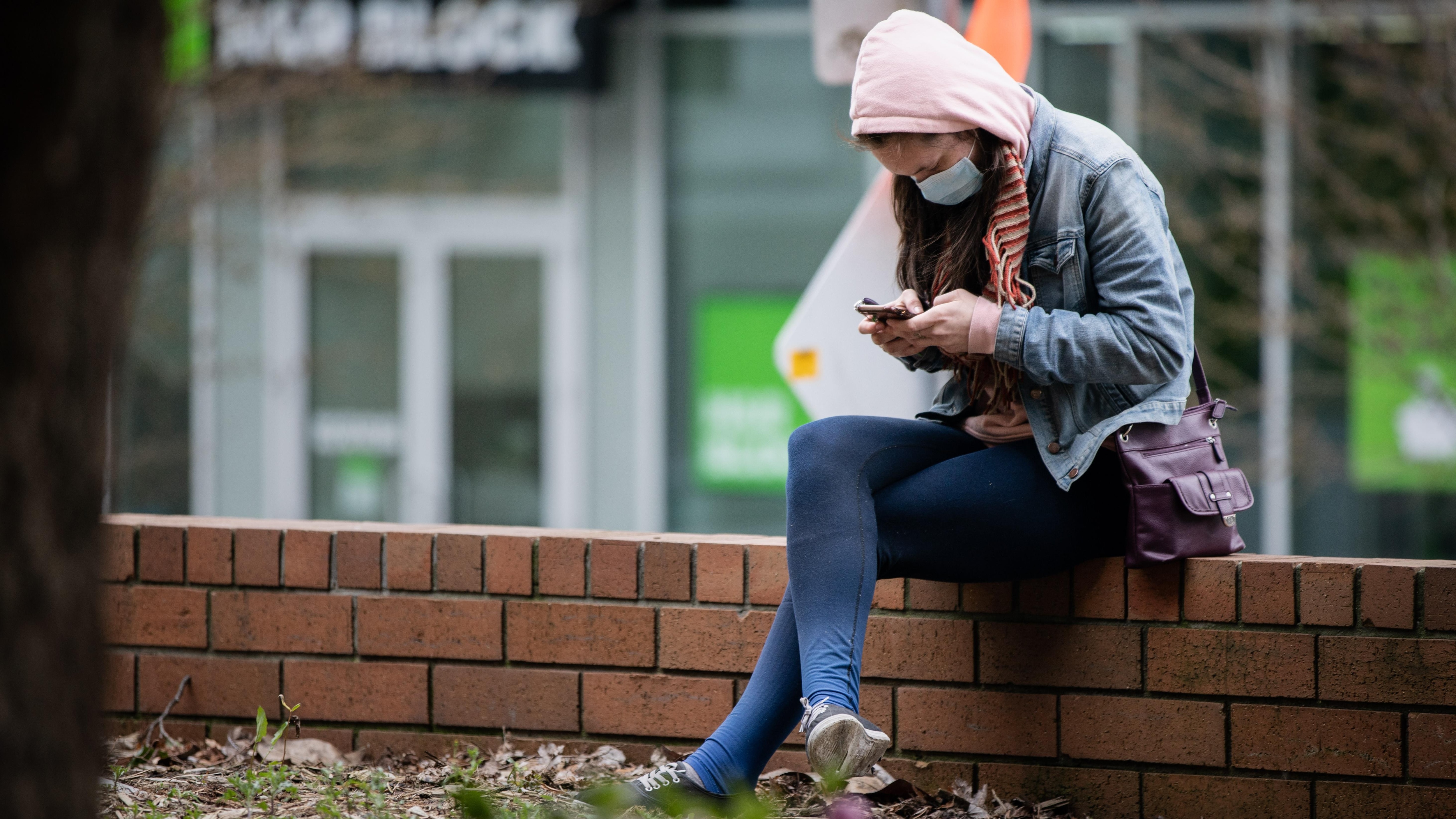 Una joven con máscara revisa sus mensajes en su teléfono celular. 