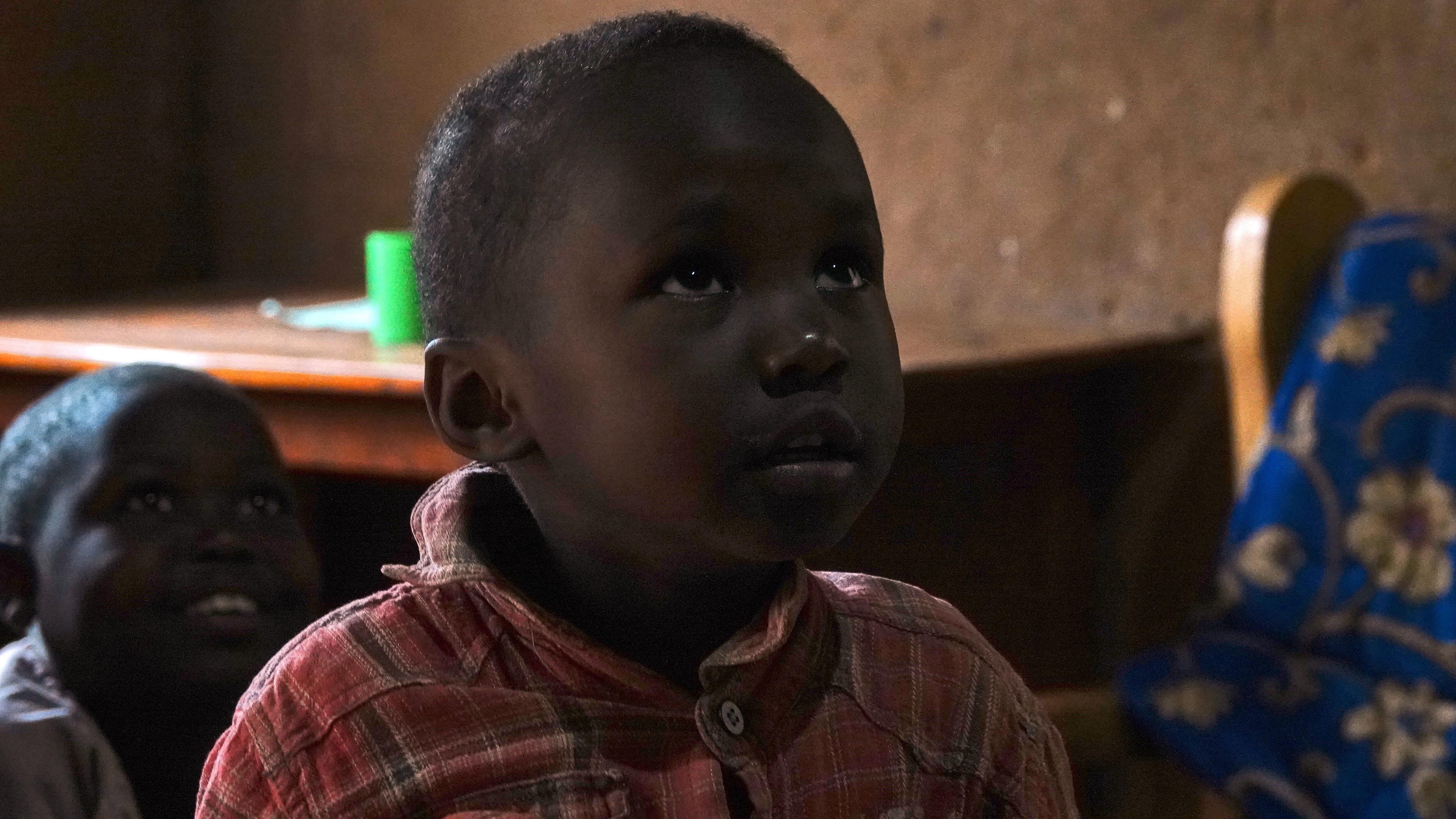 Un enfant rwandais impressionné par la lumière électrique à l'intérieur de sa maison.