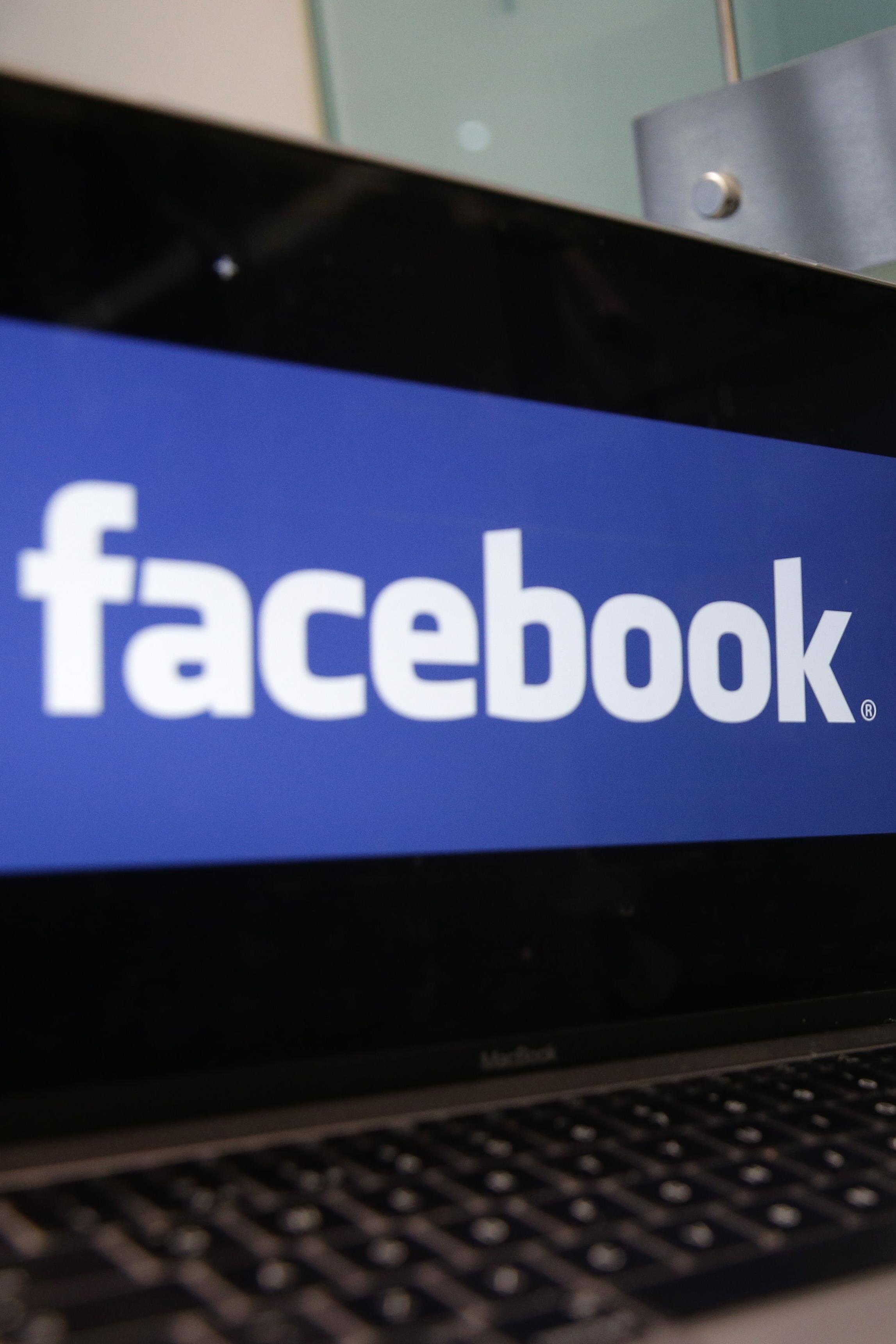 Un ordinateur portable affichant le logo de Facebook est posé à côté d'un panneau de Cambridge Analytica indiquant l'entrée des bureaux de l'entreprise à Londres, le 21 mars 2018.
