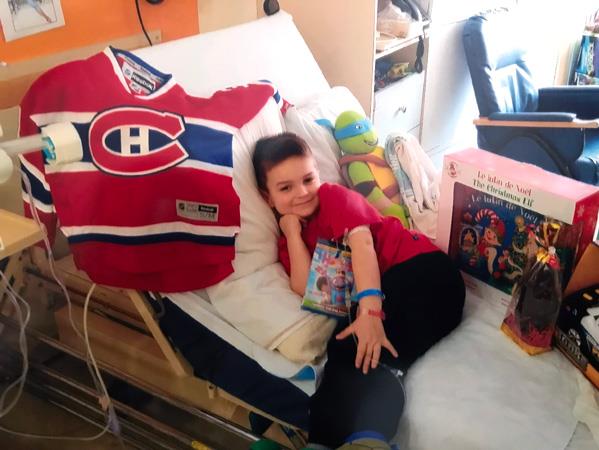 Guillaume dans son lit d’hôpital avec des jouets et un chandail du Canadien de Montréal