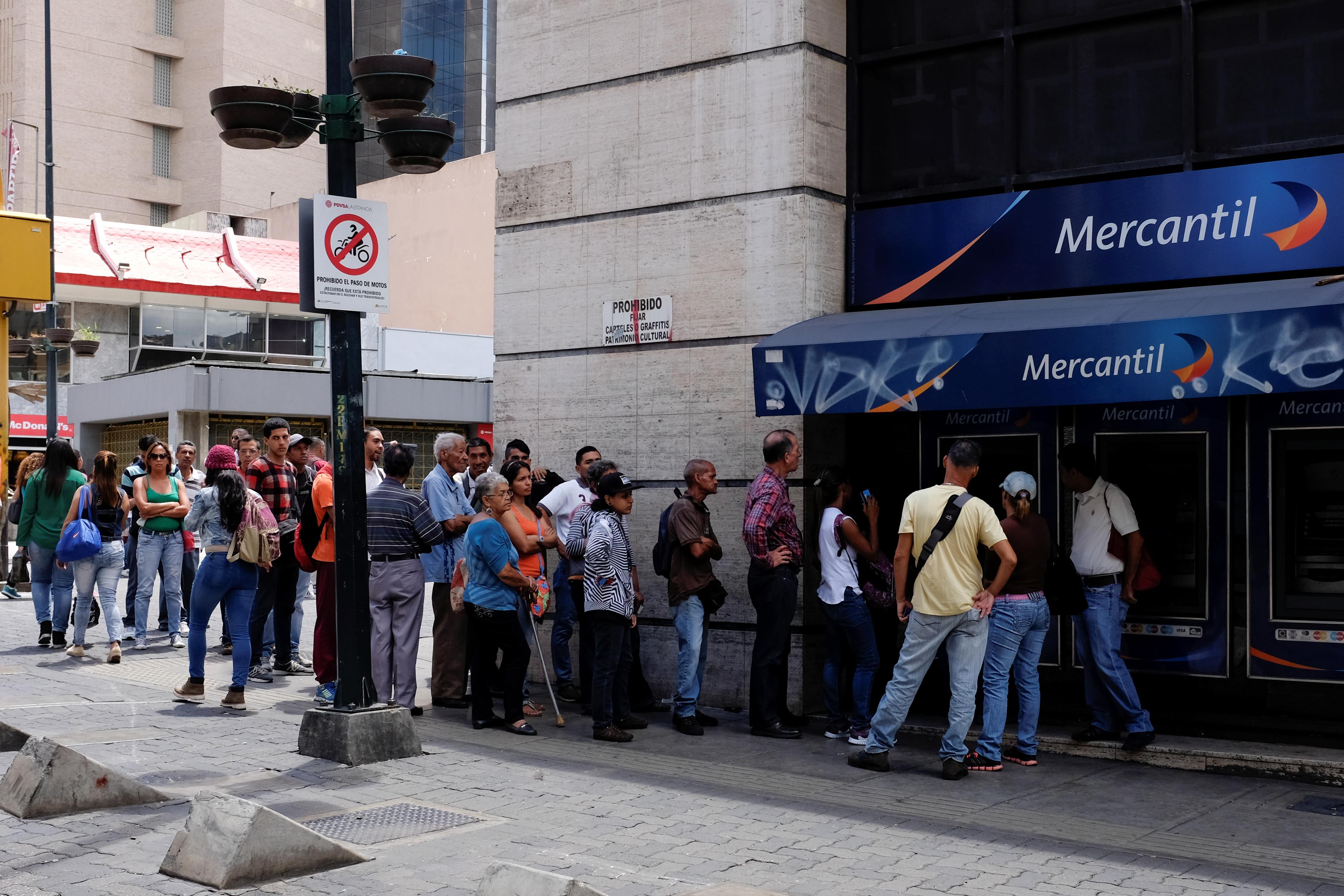 Des gens font la file pour effectuer un retrait d'un guichet automatique devant une succursale du Banco Mercantil, à Caracas, le 17 août 2018.