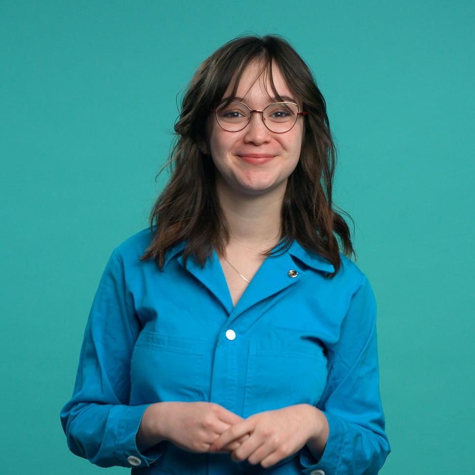Zoélie Lampron-Fournier se tient debout, souriante, devant un fond de couleur turquoise.