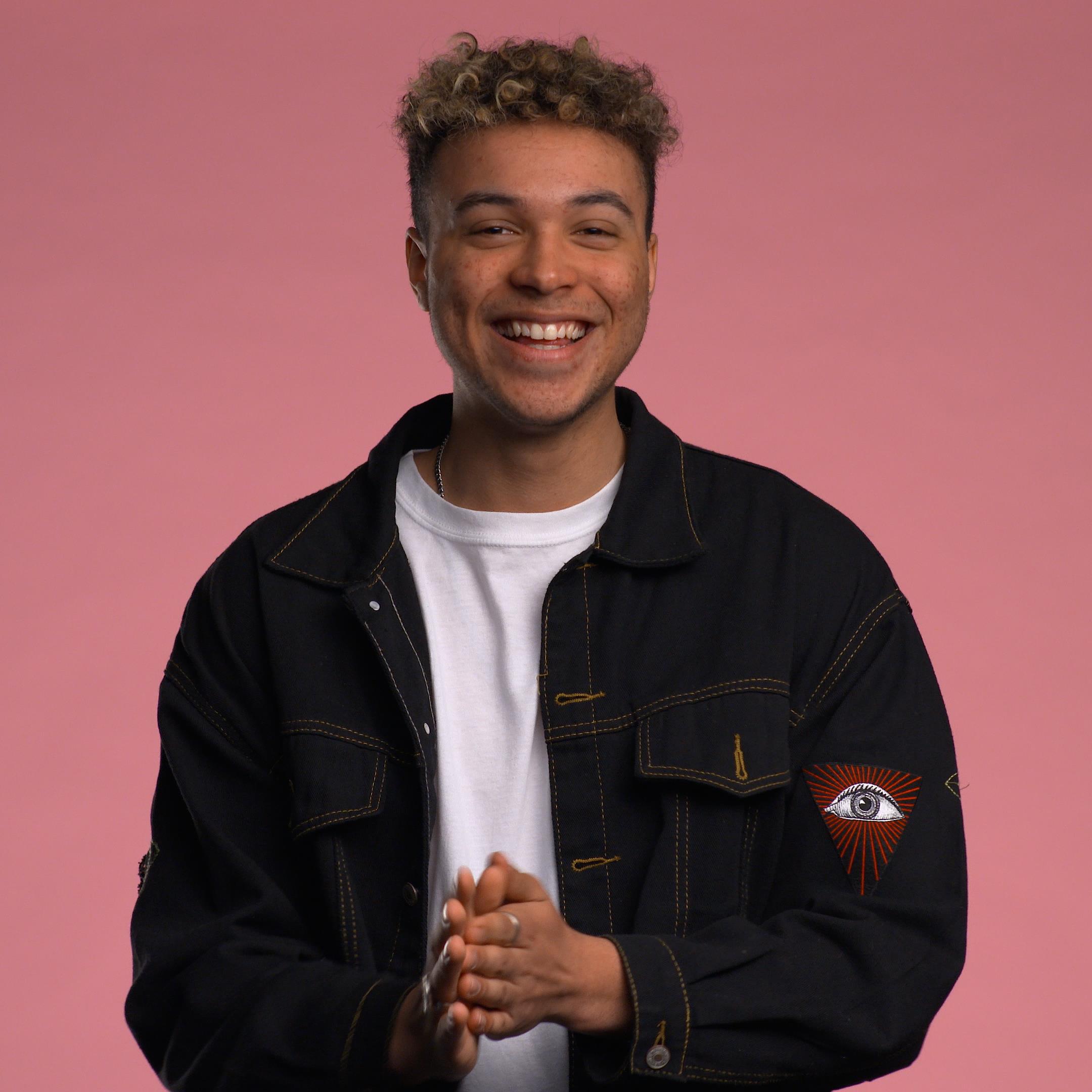 Isaac Brosseau, souriant, se tient devant un fond rose.