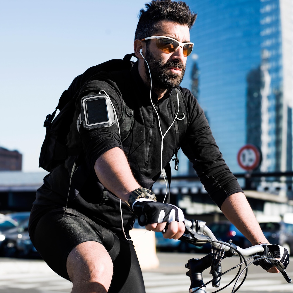 Un cycliste circule alors qu'il porte des écouteurs. Il porte aussi des verres fumés et semble se trouver en milieu urbain. Un cycliste circule alors qu'il porte des écouteurs. Il porte aussi des verres fumés et semble se trouver en milieu urbain.