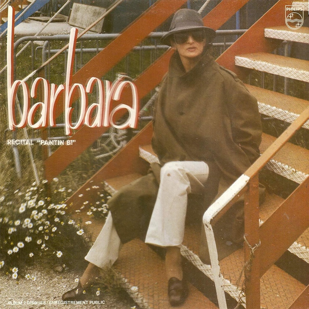 La chanteuse est assise dans des marches et porte un trench-coat brun et un chapeau. La chanteuse est assise dans des marches et porte un trench-coat brun et un chapeau.