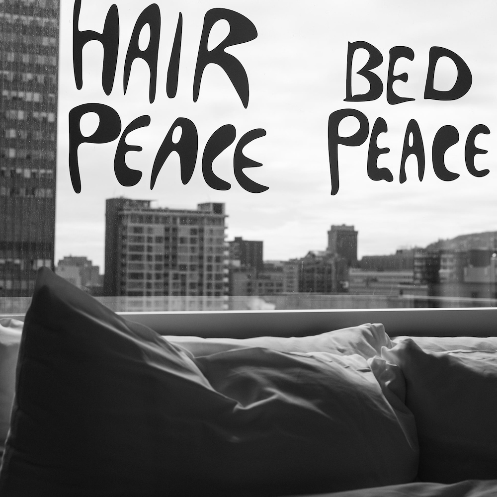 Photo en noir et blanc d'une chambre. Les mots hair peace et bed peace sont inscrits sur une fenêtre. Photo en noir et blanc d'une chambre. Les mots hair peace et bed peace sont inscrits sur une fenêtre.