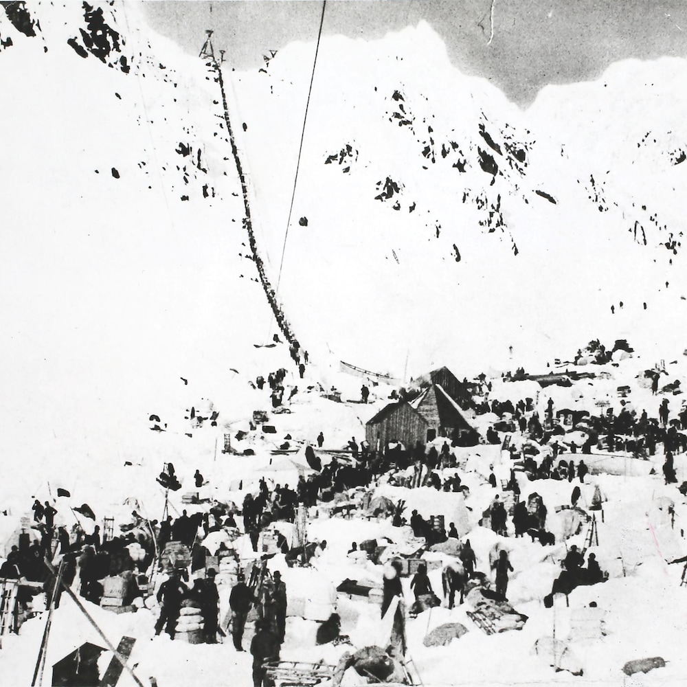 Photo en noir et blanc montrant un groupe de prospecteurs en train de faire la traversée des montagnes vers le Klondike en 1897. Photo en noir et blanc montrant un groupe de prospecteurs en train de faire la traversée des montagnes vers le Klondike en 1897.