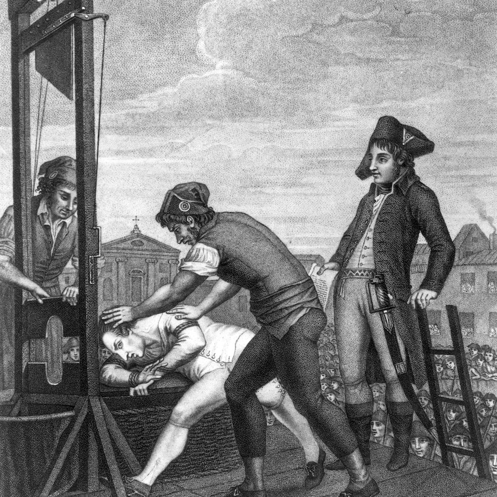 Dessin en noir et blanc de deux hommes qui en placent un autre sur une guillotine, tandis qu'un troisième les regarde. Dessin en noir et blanc de deux hommes qui en placent un autre sur une guillotine, tandis qu'un troisième les regarde.