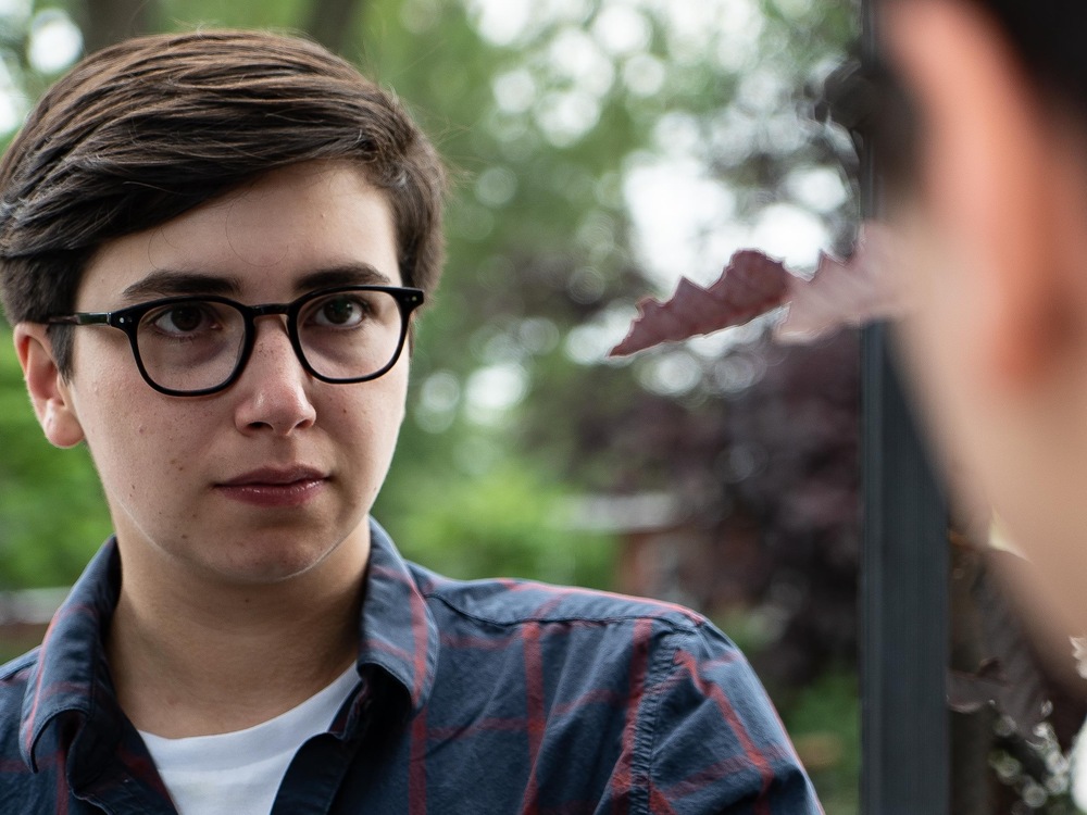 On voit Adam, de face, qui se regarde dans un miroir. Il porte des lunettes.