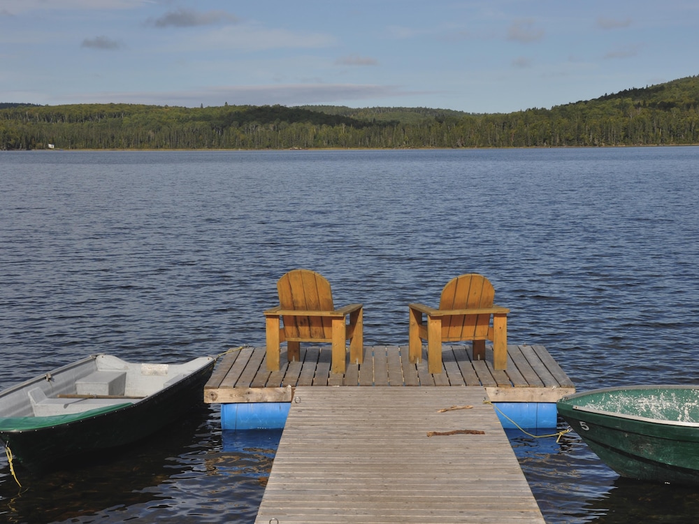 Deux fauteuils Adirondack se trouvent sur le quai d’un lac en Haute-Mauricie. Deux chaloupes flottent de chaque côté.