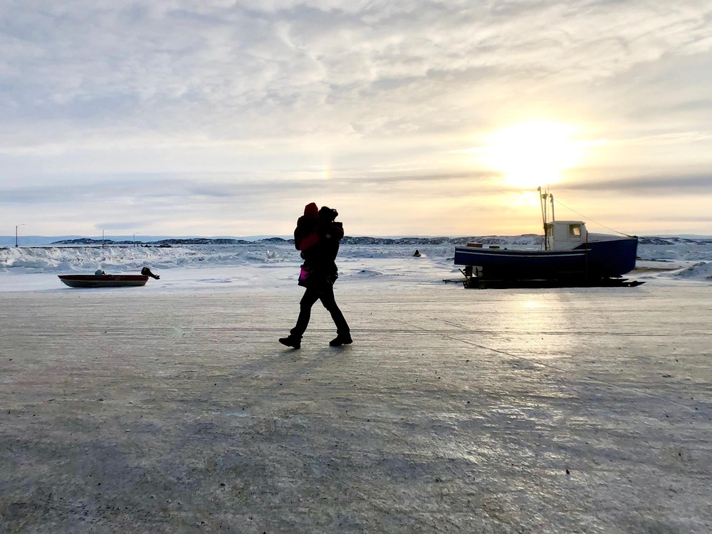 Une mère marche avec son enfant dans les bras à proximité de la baie de Frobisher, à Iqaluit.