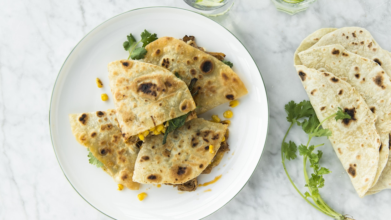 Plusieurs quesadillas au porc braisé accompagné de maïs dans une assiette. 
