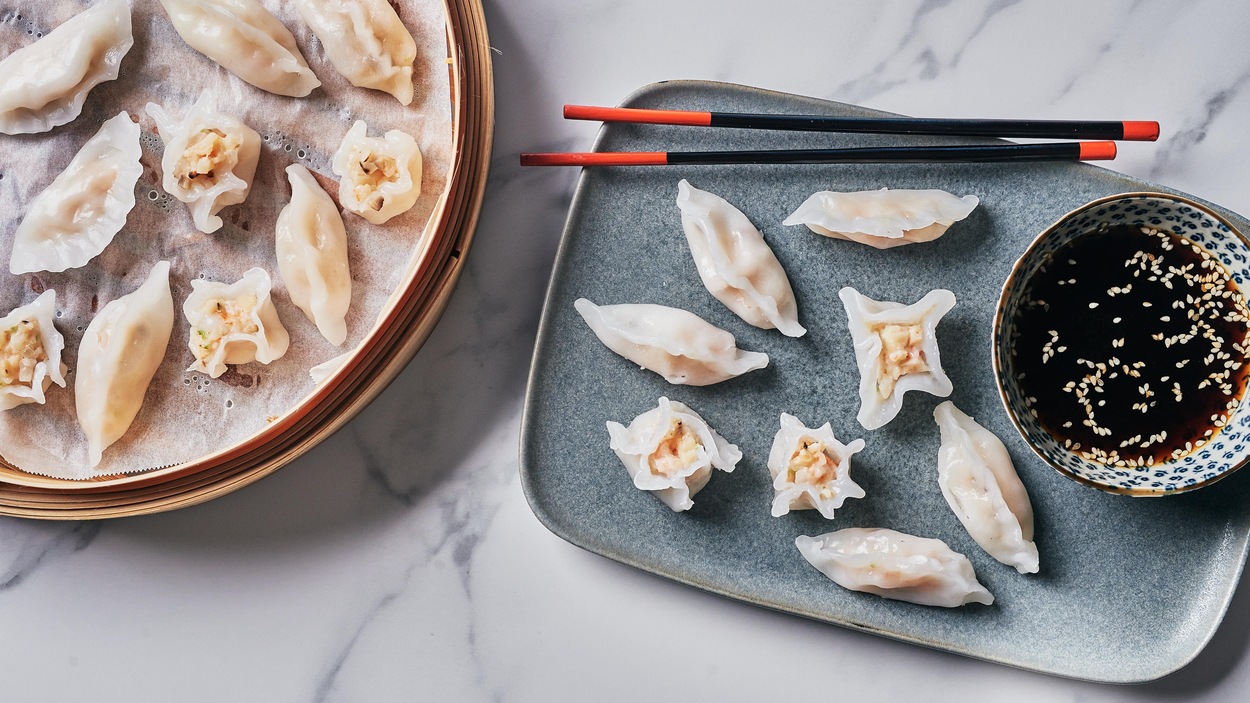 Des dim sums aux fruits de mer dans une assiette servis avec de la sauce soya.