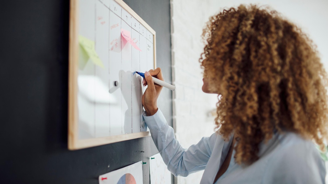 Une femme de profil est en train d'écrire son horaire sur un tableau. Une femme de profil est en train d'écrire son horaire sur un tableau.