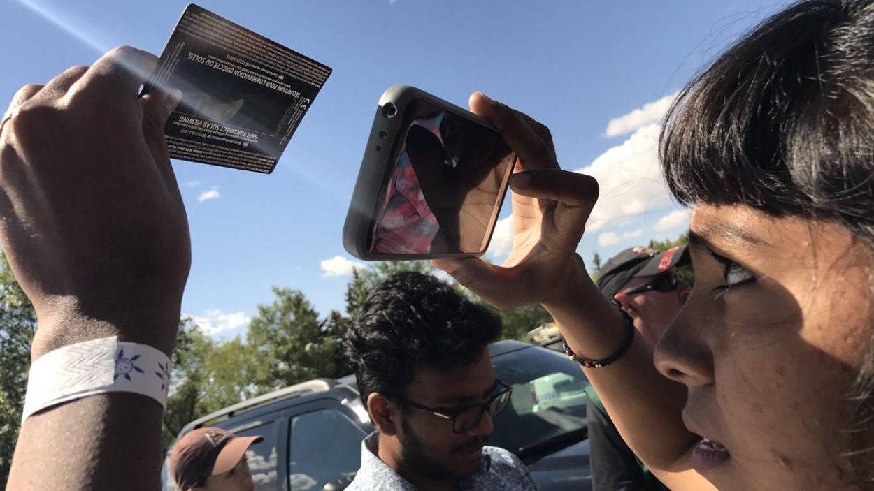 Une femme regarde l'éclipse solaire à travers son téléphine cellulaire. Une femme regarde l'éclipse solaire à travers son téléphine cellulaire.