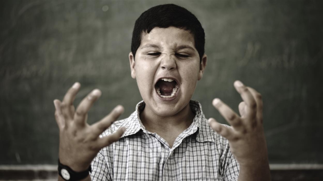Un enfant debout devant un tableau d'école, la bouche grande ouverte pour crier et les yeux plissés de rage lève les mains, paumes vers le ciel. Un enfant debout devant un tableau d'école, la bouche grande ouverte pour crier et les yeux plissés de rage lève les mains, paumes vers le ciel.
