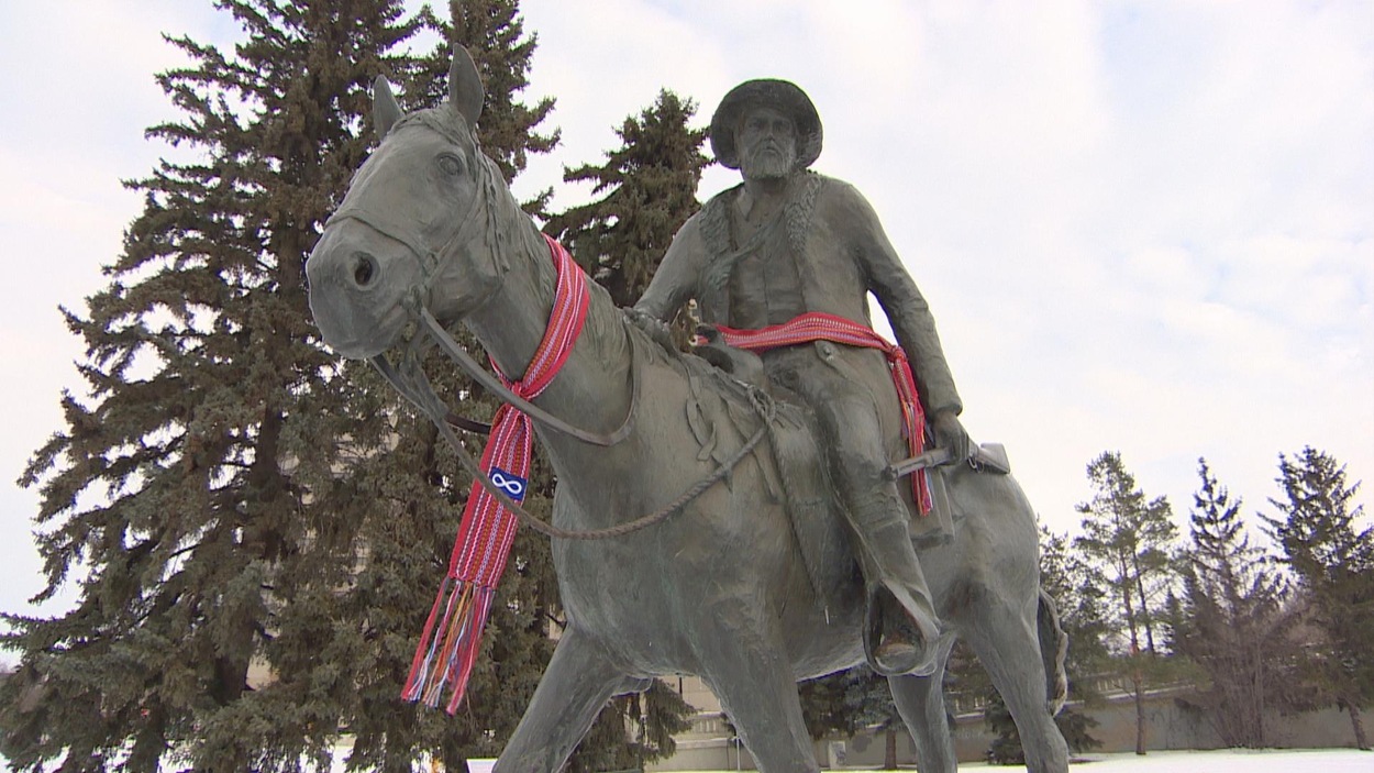 La statue de Gabriel Dumont revêt deux ceintures fléchées aux insignes métis. La statue de Gabriel Dumont revêt deux ceintures fléchées aux insignes métis.