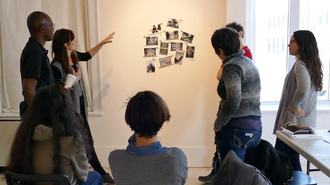 L'artiste Dominique Rey pointe et parle aux participants au sujet des photos accrochées au mur. L'artiste Dominique Rey pointe et parle aux participants au sujet des photos accrochées au mur.