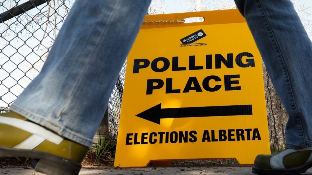 Une pancarte jaune indiquant la direction d'un bureau de vote est posée sur un trottoir. On aperçoit les jambes d'un passant qui se dirige vers ce lieu. Une pancarte jaune indiquant la direction d'un bureau de vote est posée sur un trottoir. On aperçoit les jambes d'un passant qui se dirige vers ce lieu.