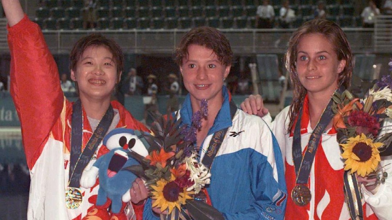 Trois femmes en survêtement avec une médaille au cou posent pour les photographes devant une piscine olympique. Trois femmes en survêtement avec une médaille au cou posent pour les photographes devant une piscine olympique.